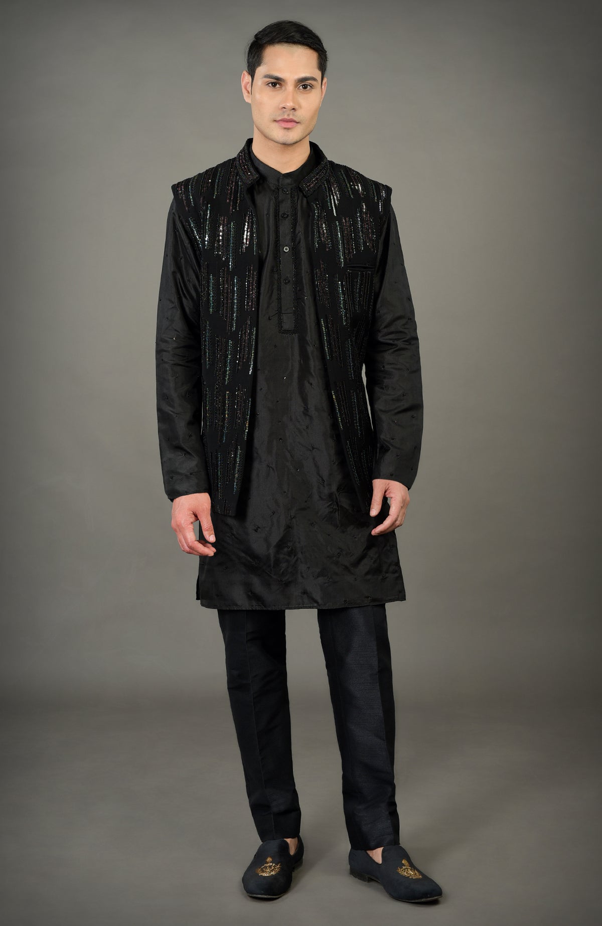 A man models a black hand-embroidered jacket set with a kurta and trousers.