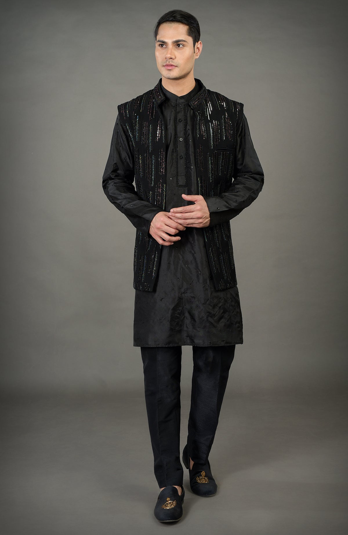 A man models a black hand-embroidered jacket set with a kurta and trousers.