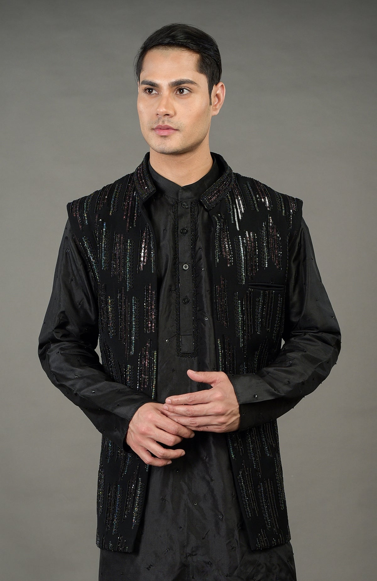 A man models a black hand-embroidered jacket set with a matching kurta and trousers.