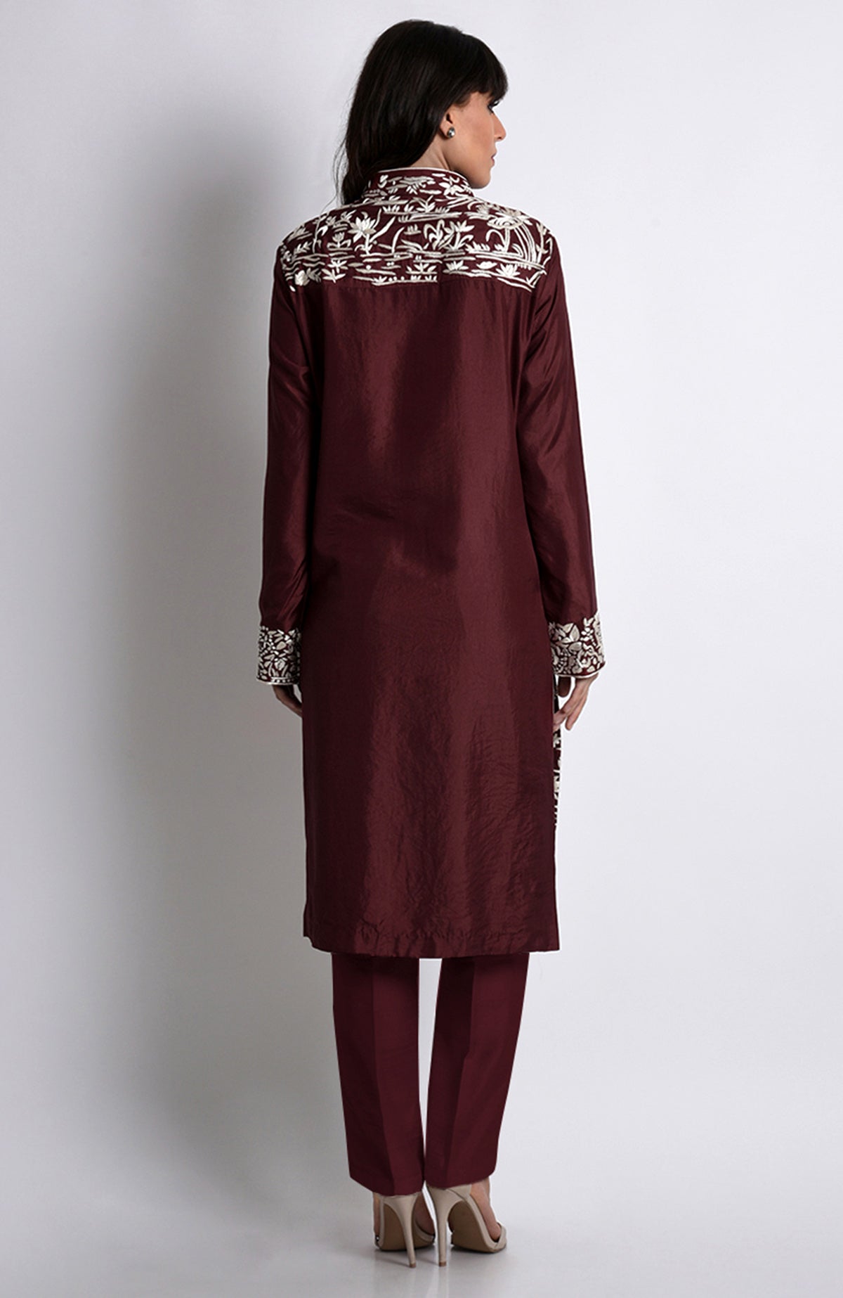 A woman models a maroon Parsi Gara embroidered jacket set with ivory floral and crane-bird patterns.
