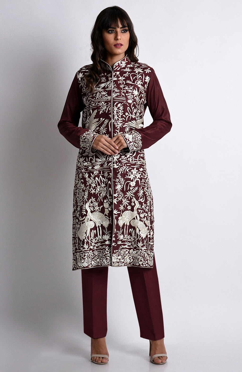A woman models a maroon Parsi Gara embroidered jacket set with ivory floral and crane designs.
