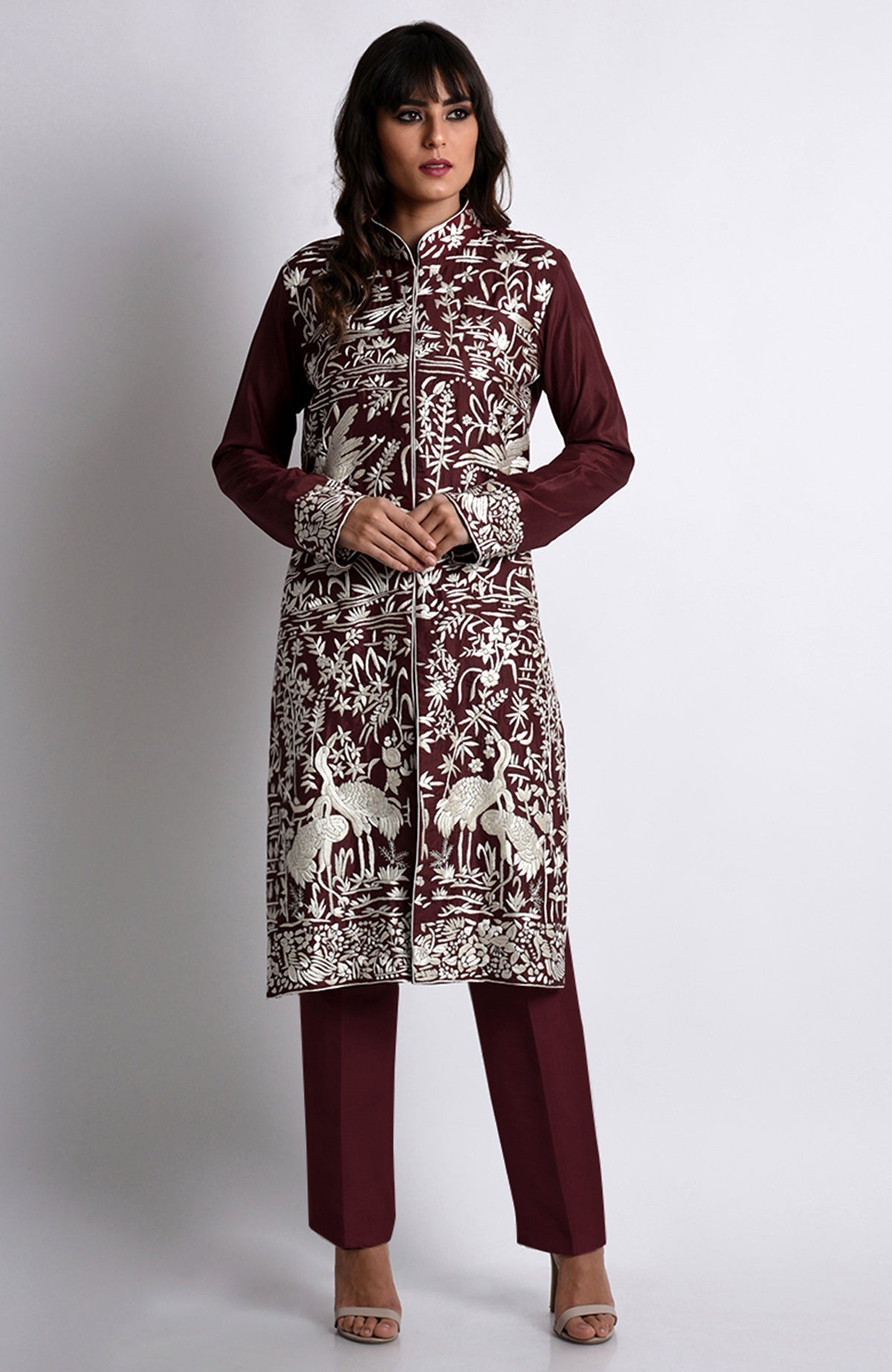 A woman models a maroon Parsi Gara embroidered jacket set with ivory floral and crane designs.