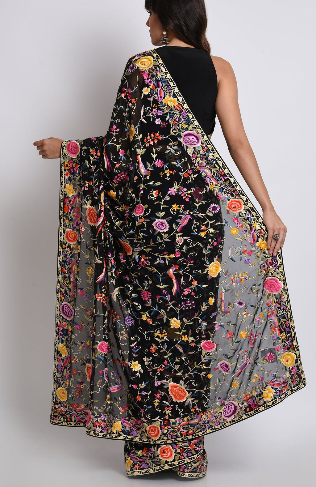 A woman models a black Parsi Gara hand-embroidered saree with colorful floral and bird patterns.