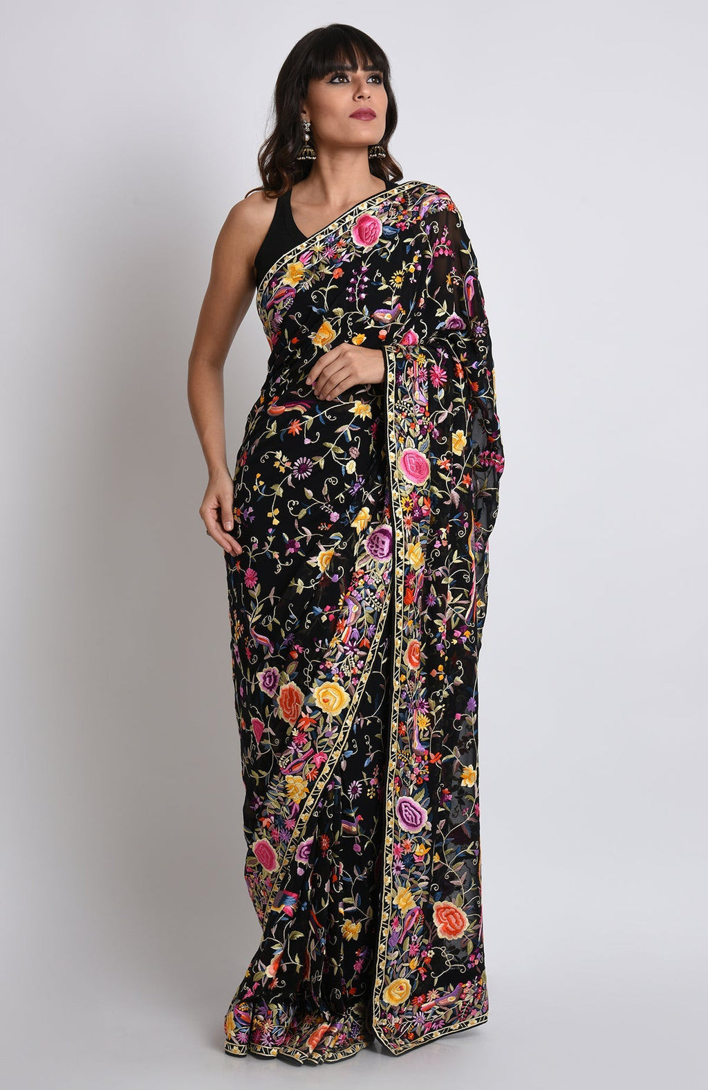 A woman models a black Parsi Gara hand-embroidered saree with colorful floral and bird motifs.