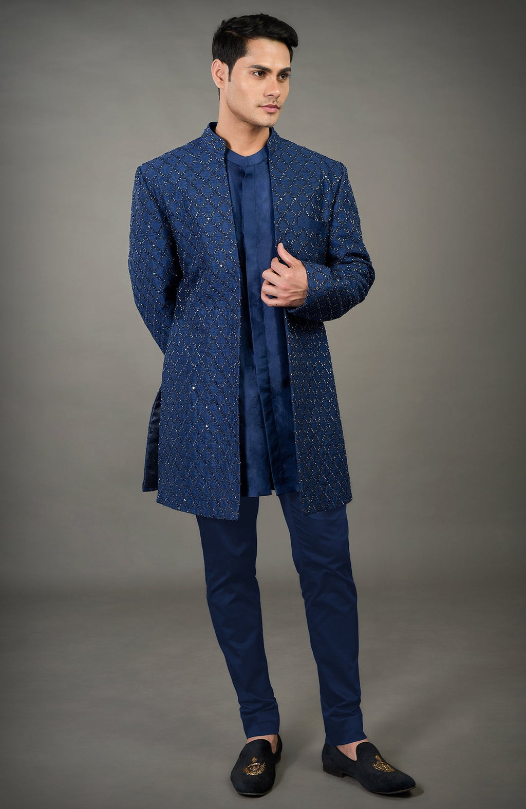 A man models a navy blue chikankari embellished jacket set with matching pants and loafers.