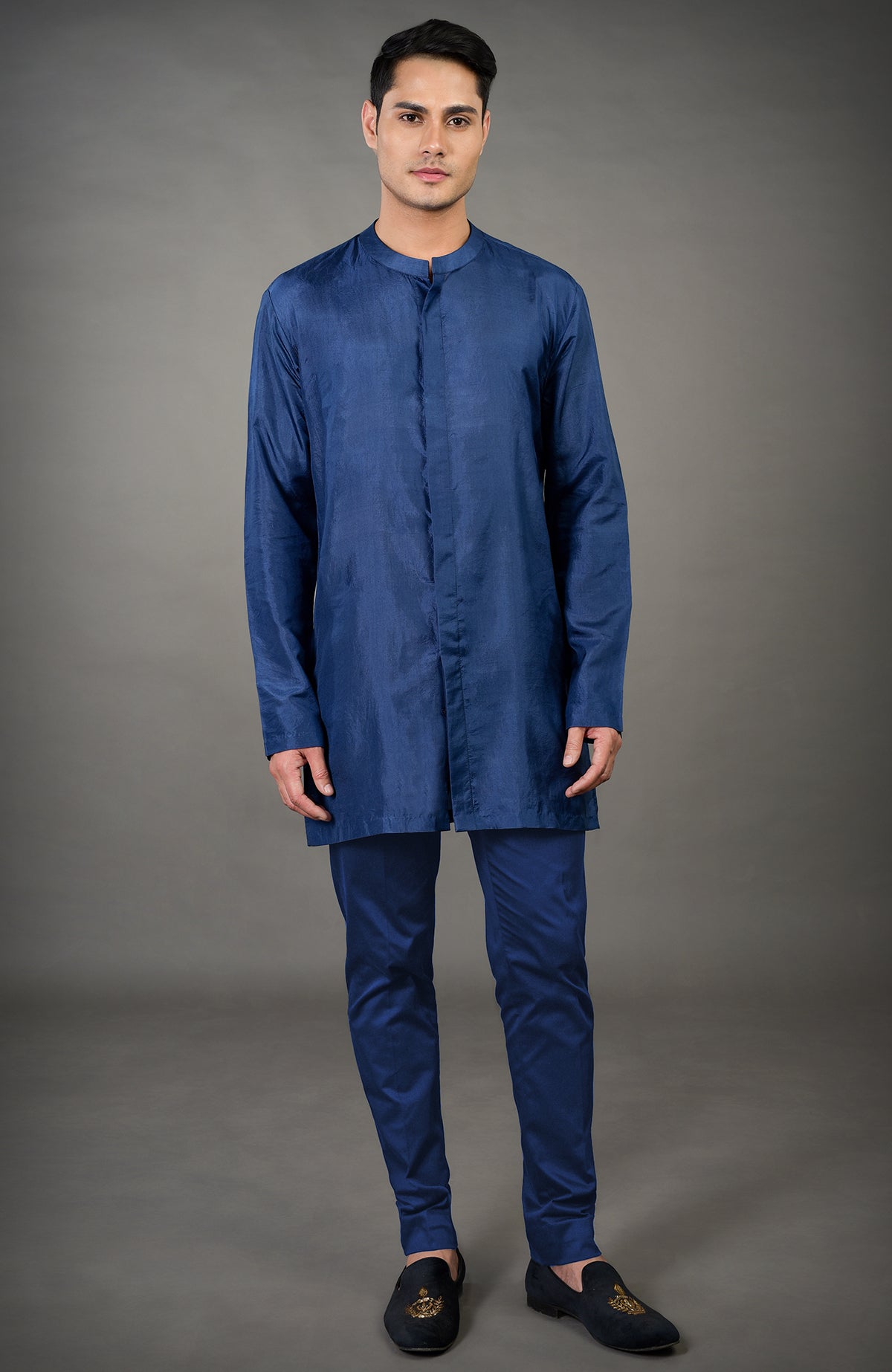 A man models a navy blue chikankari embellished jacket set with tailored pants and black loafers.