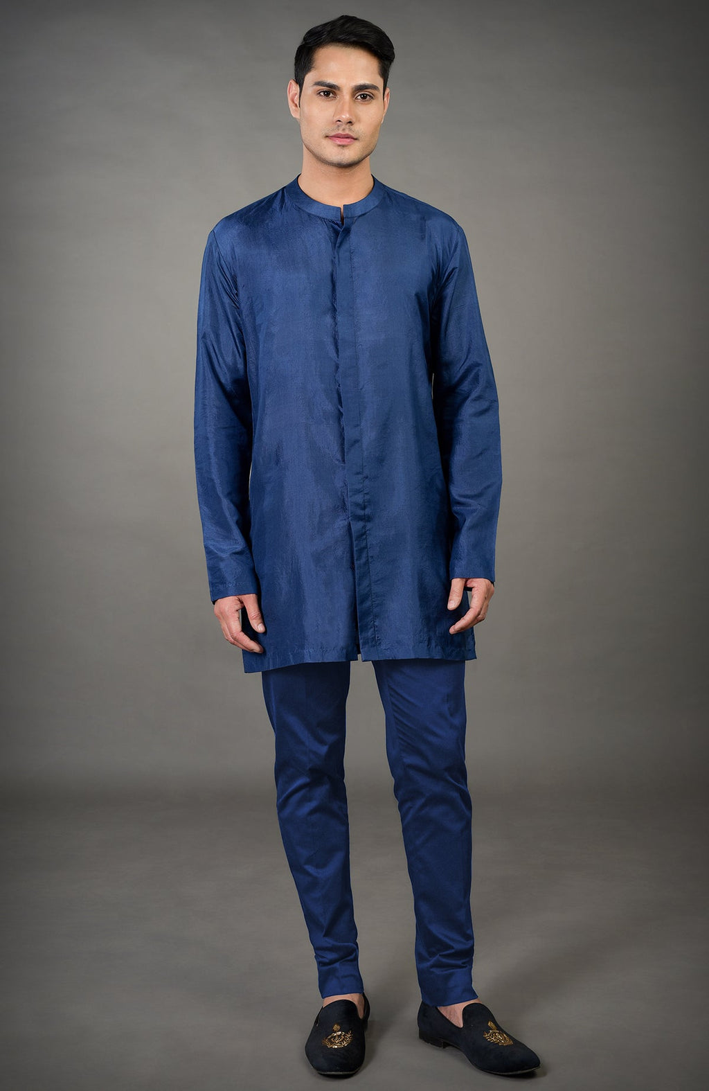 A man models a navy blue chikankari embellished jacket set with tailored pants and black loafers.
