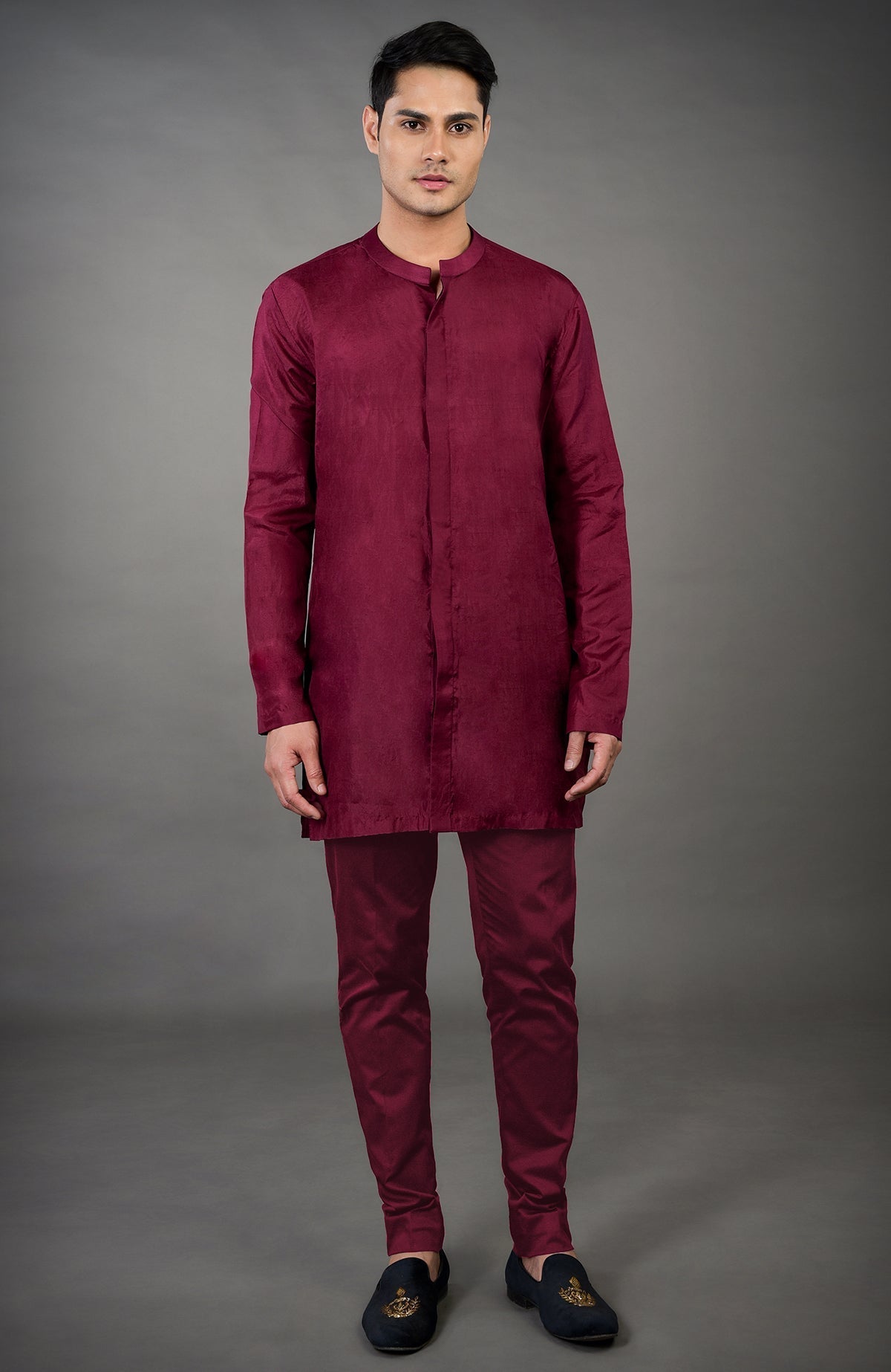 A man models a maroon chikankari embellished jacket set with black embroidered loafers.