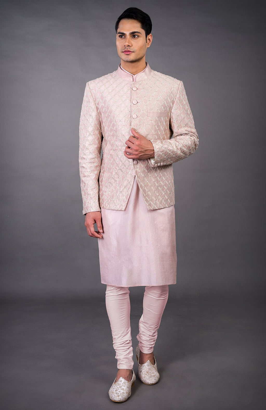 A man models a barely pink chikankari embellished bandhgala set with matching kurta and pants.
