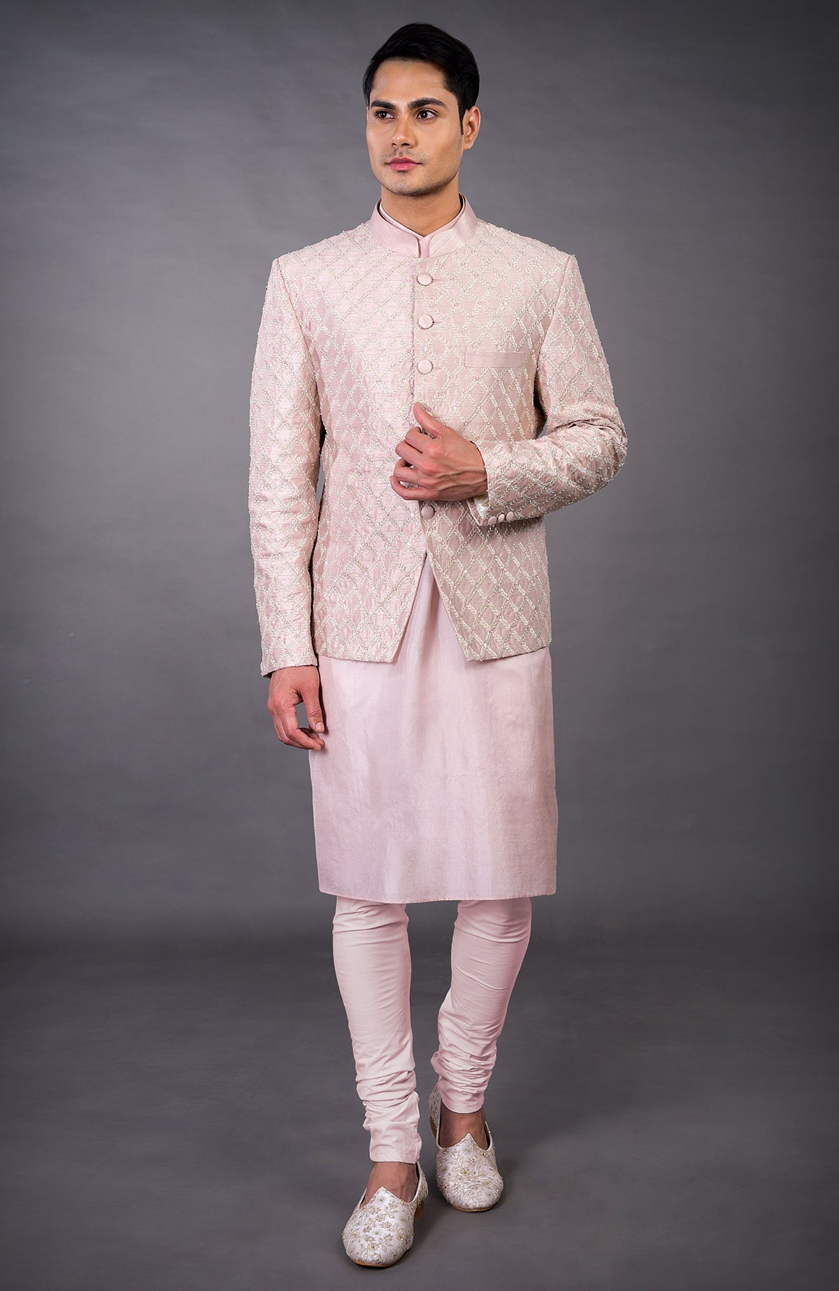 A man models a barely pink chikankari embellished bandhgala set with matching kurta and pants.