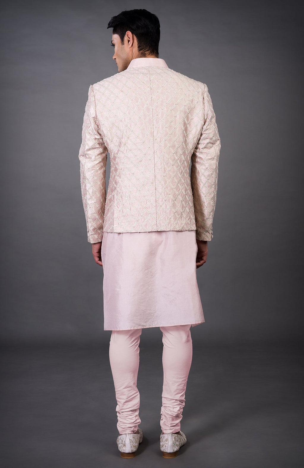 A man from behind wears a barely pink chikankari embellished bandhgala set.