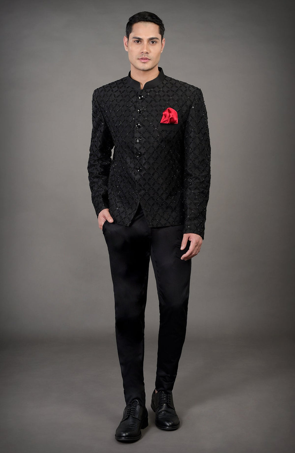 A man models a black chikankari embellished jacket set with a red pocket square.