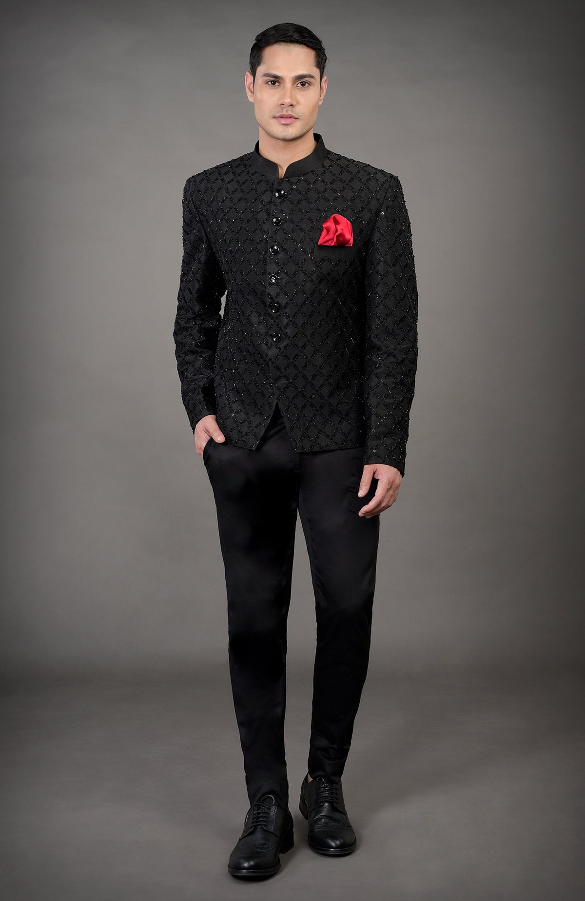 A man models a black chikankari embellished jacket set with a red pocket square.
