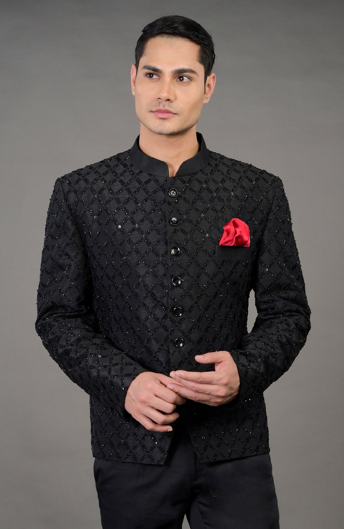 A man models a black chikankari embellished jacket set with a red pocket square.