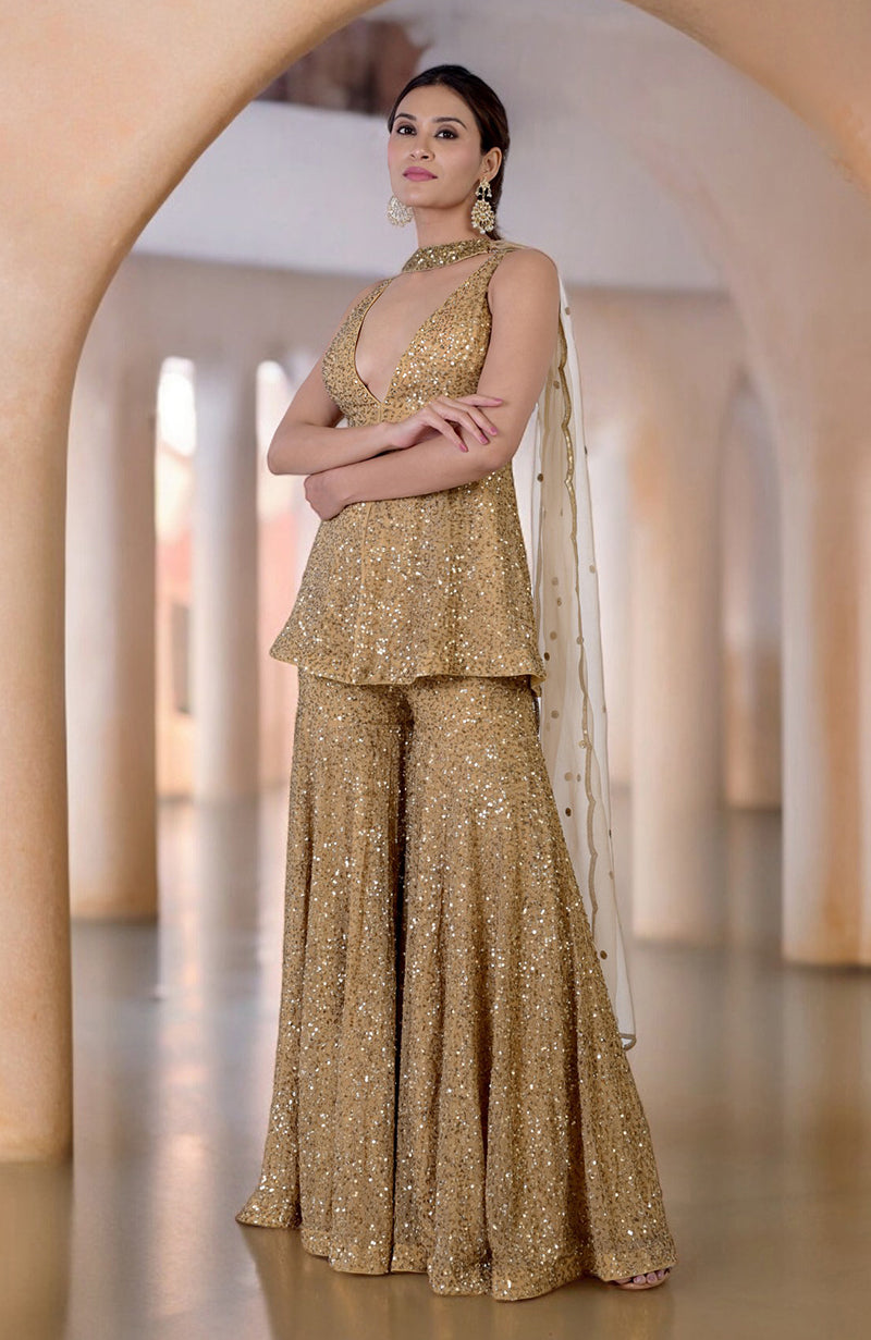 A woman models a gold sequin sharara set with a plunging neckline and matching pants.