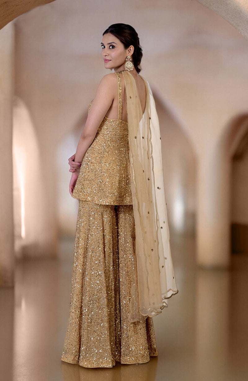 A woman in a gold sequin sharara set with a matching dupatta.