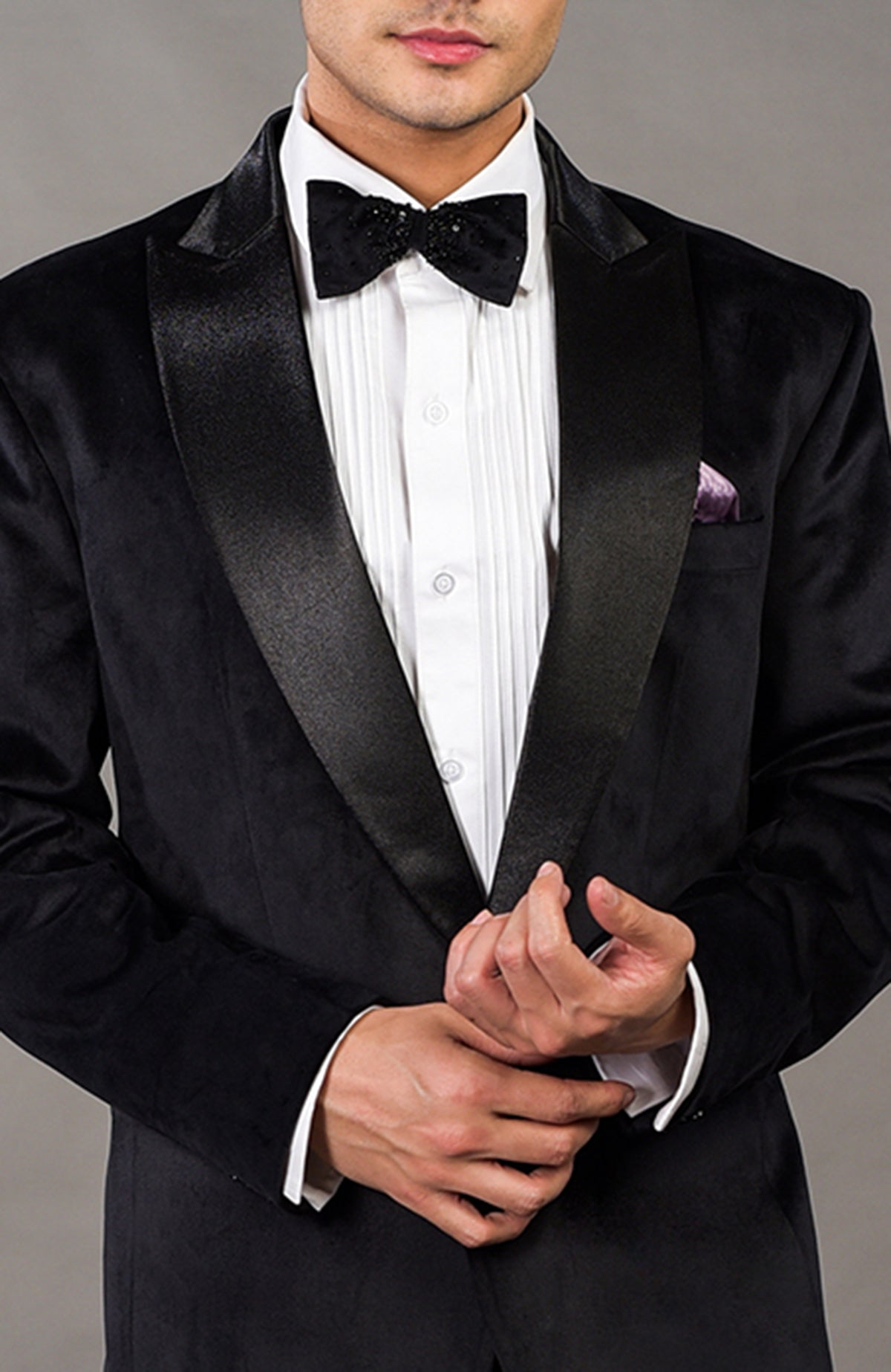 A man models a black velvet tuxedo jacket with a white pleated shirt and black bow tie.