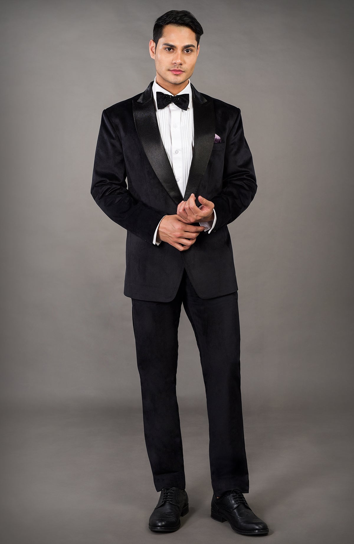 A man models a black velvet tuxedo with a white shirt and black bow tie.