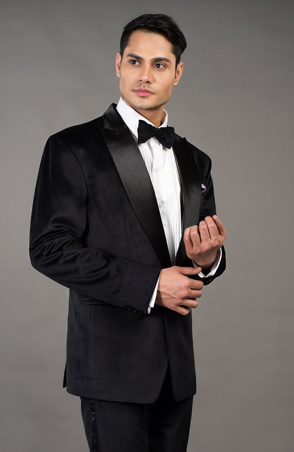 A man models a solid black velvet tuxedo set with a white shirt and black bow tie.