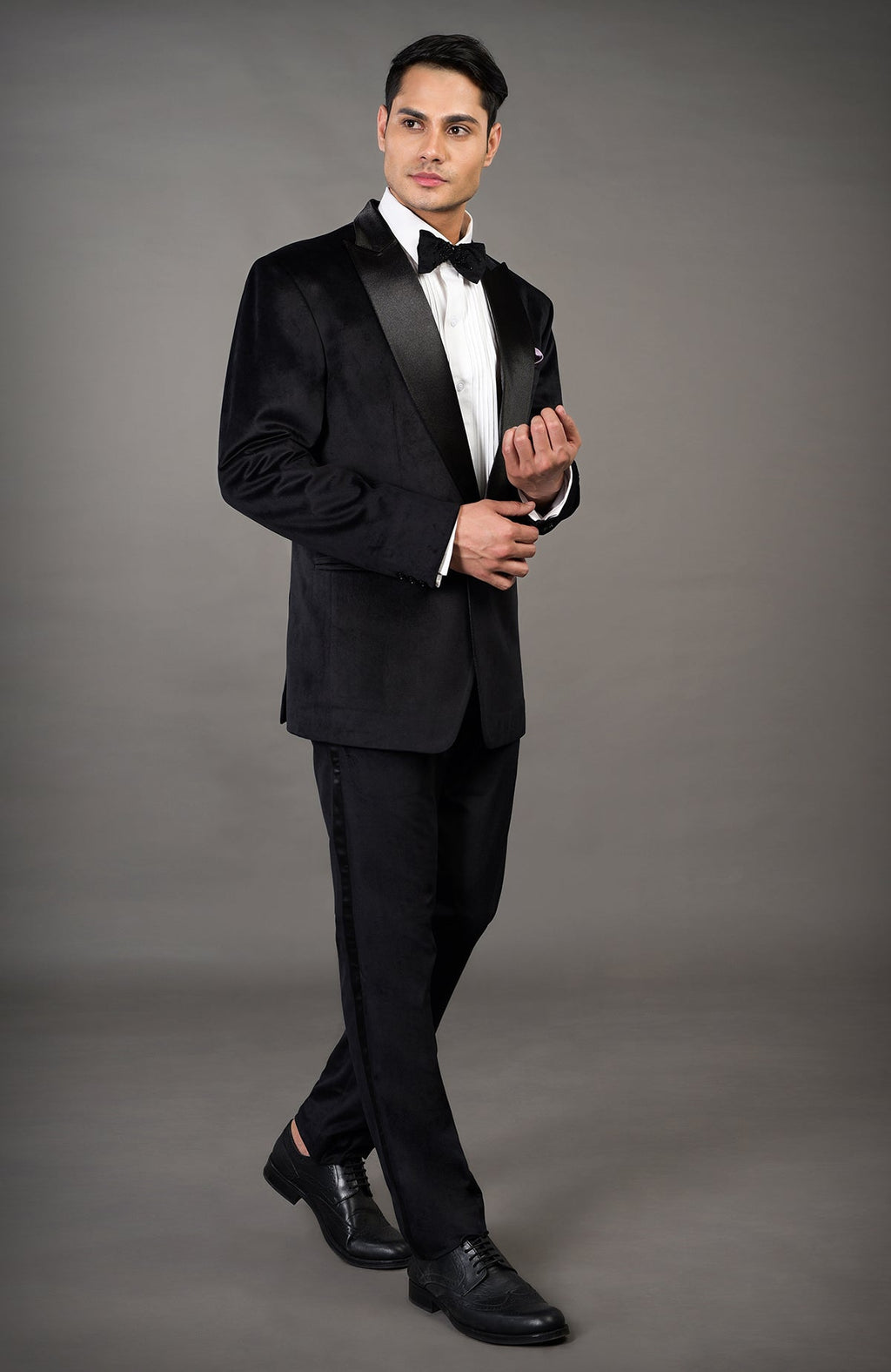 A man models a black velvet tuxedo set with a white shirt and black bow tie.