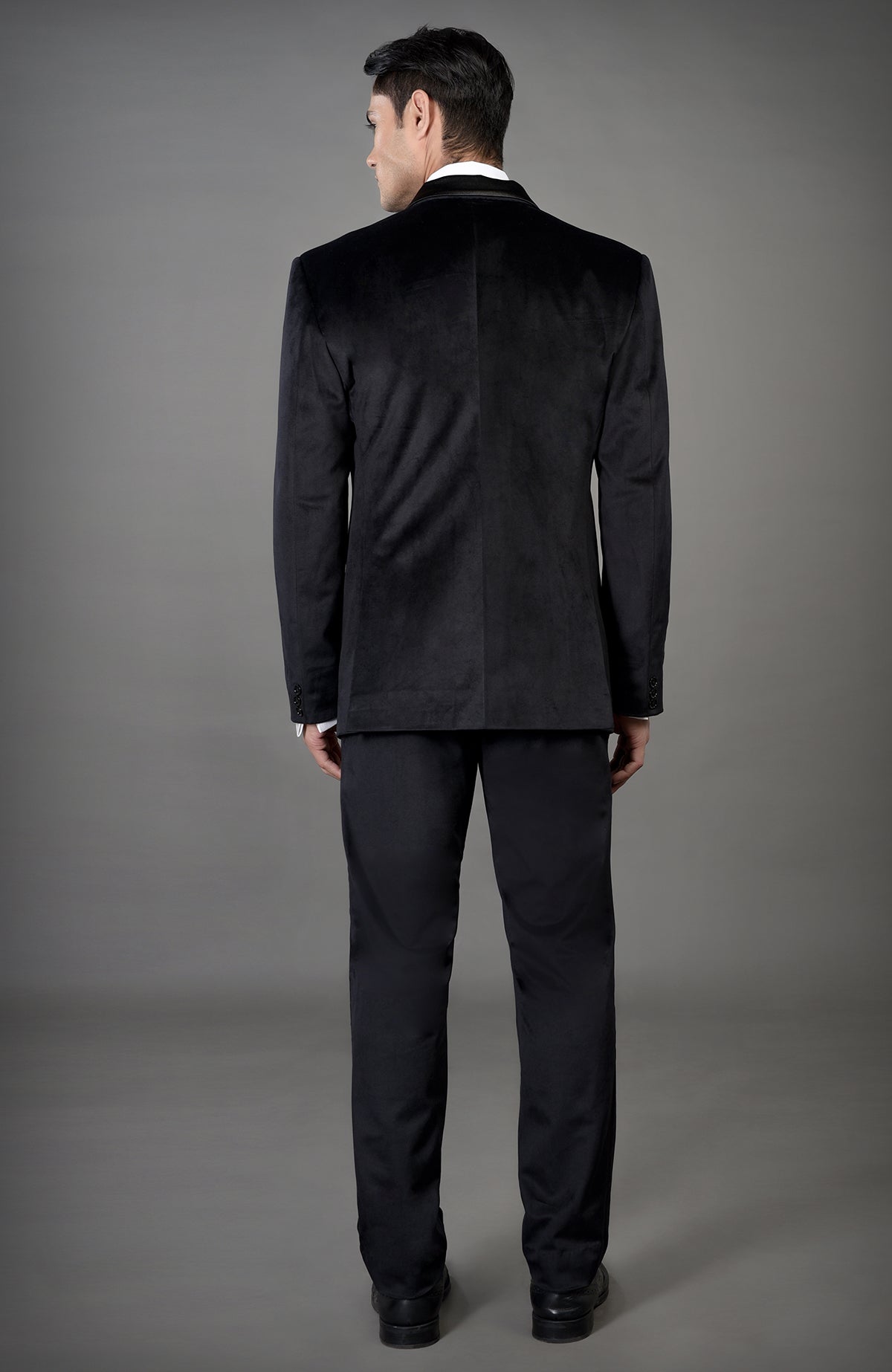 A man in a black velvet tuxedo set, seen from the back.