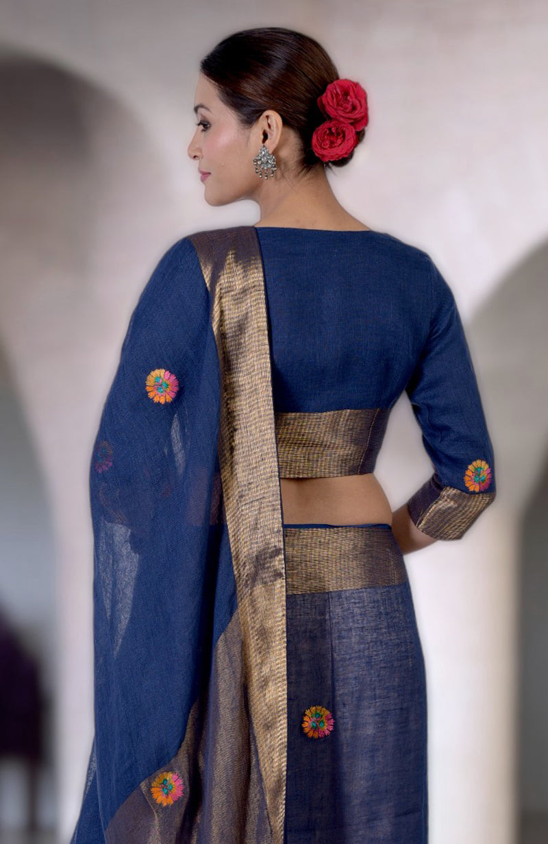 Woman in a navy blue linen saree with gold zari and colorful floral embroidery.