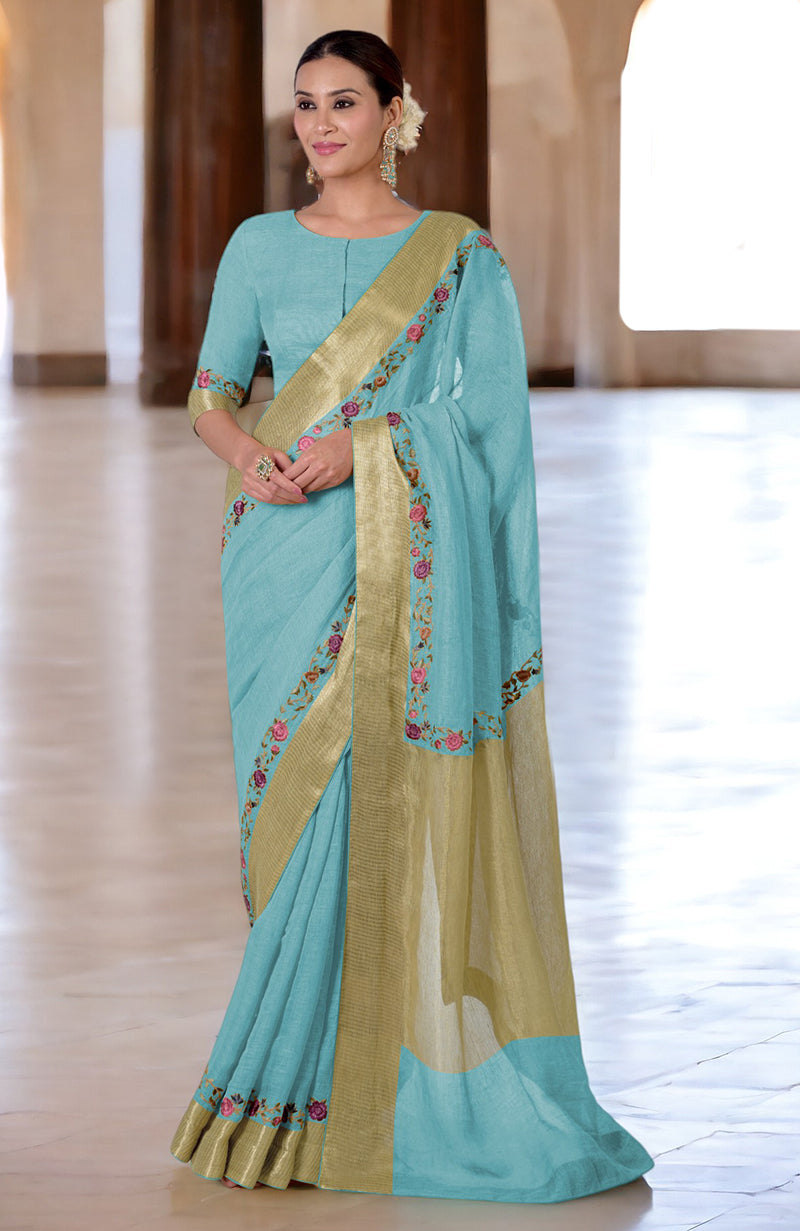A woman models a light blue linen saree with gold borders and floral embroidery.
