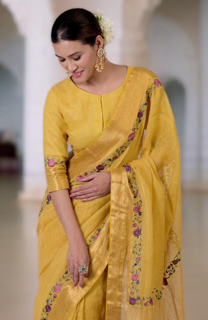A woman in a calendula yellow Parsi Gara embroidered linen saree with a matching blouse.
