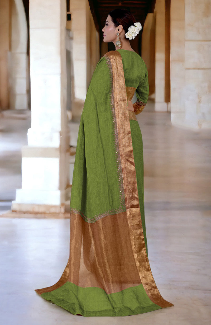 A woman in a green linen saree with gold embroidered borders stands in a hallway.