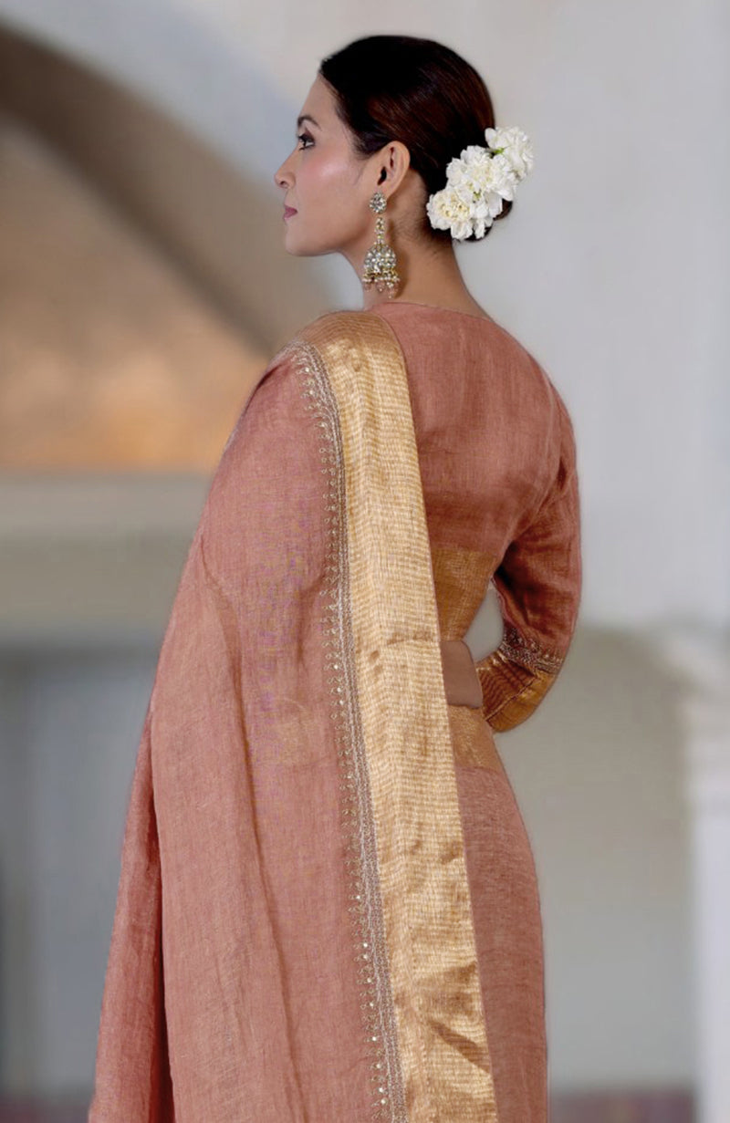 A woman in a chutney-colored linen saree with gold marori embroidered borders.