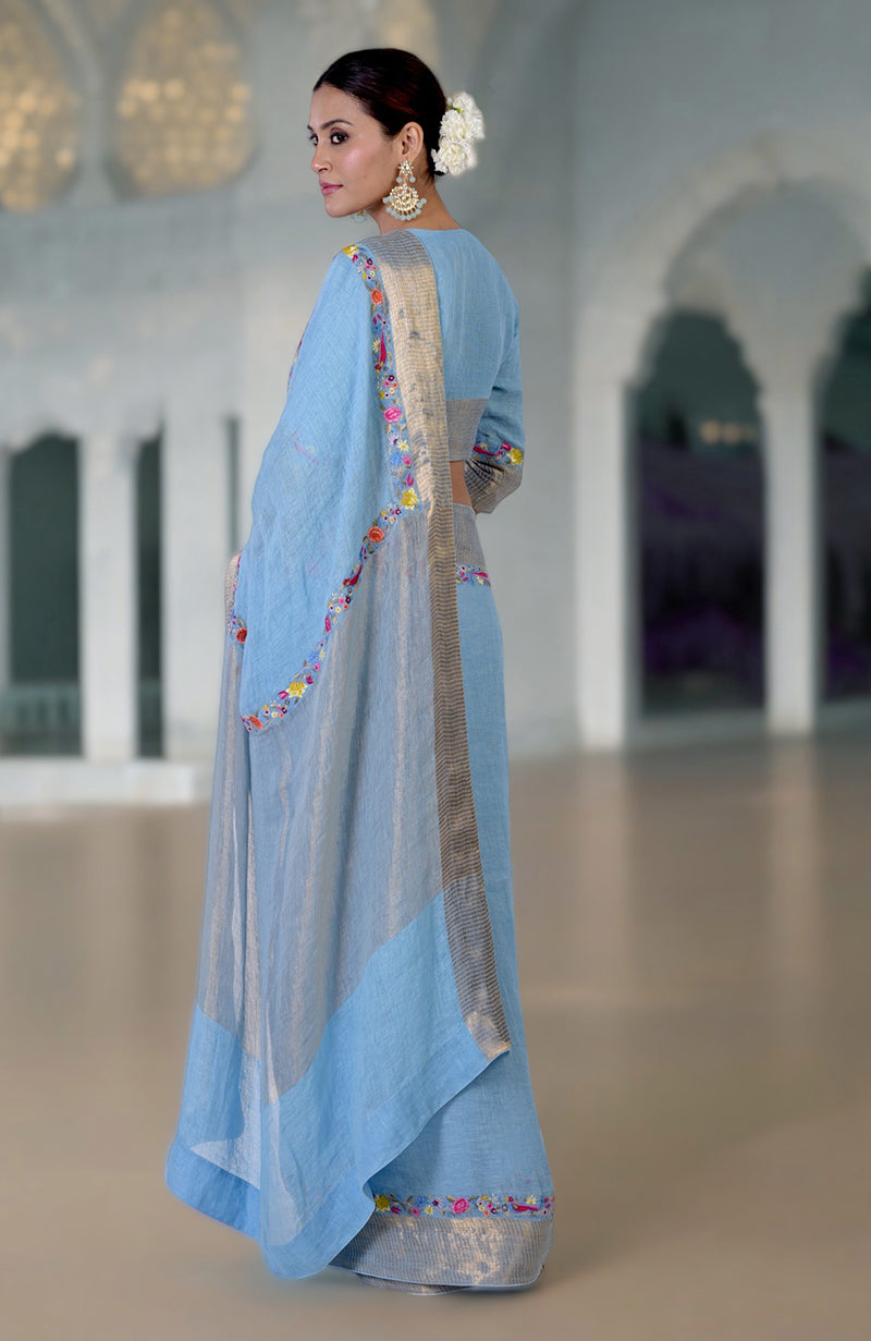 A woman in a cerulean blue Parsi Gara embroidered linen saree with zari details.