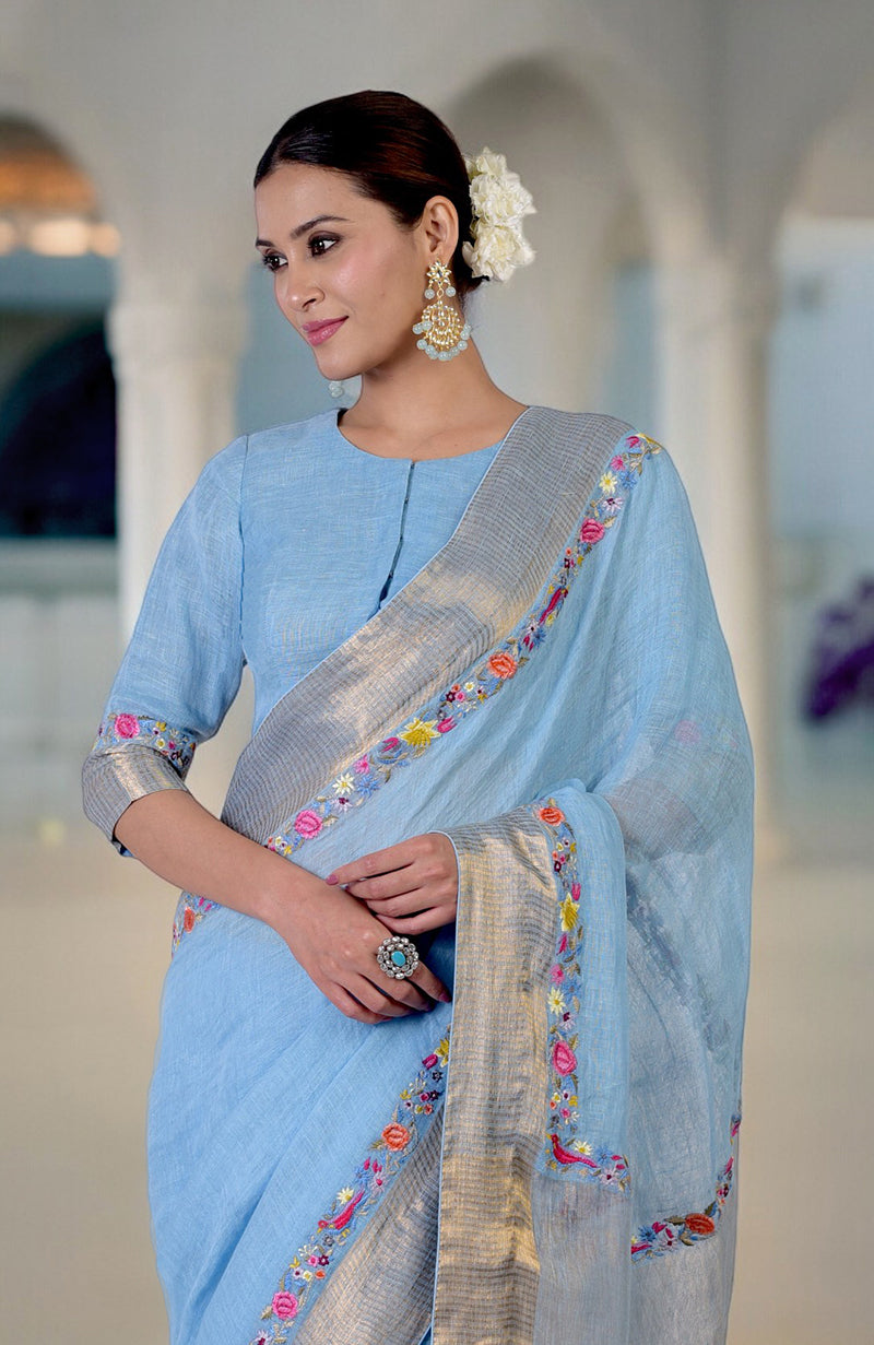 A woman in a cerulean blue linen saree with Parsi Gara embroidery and zari.