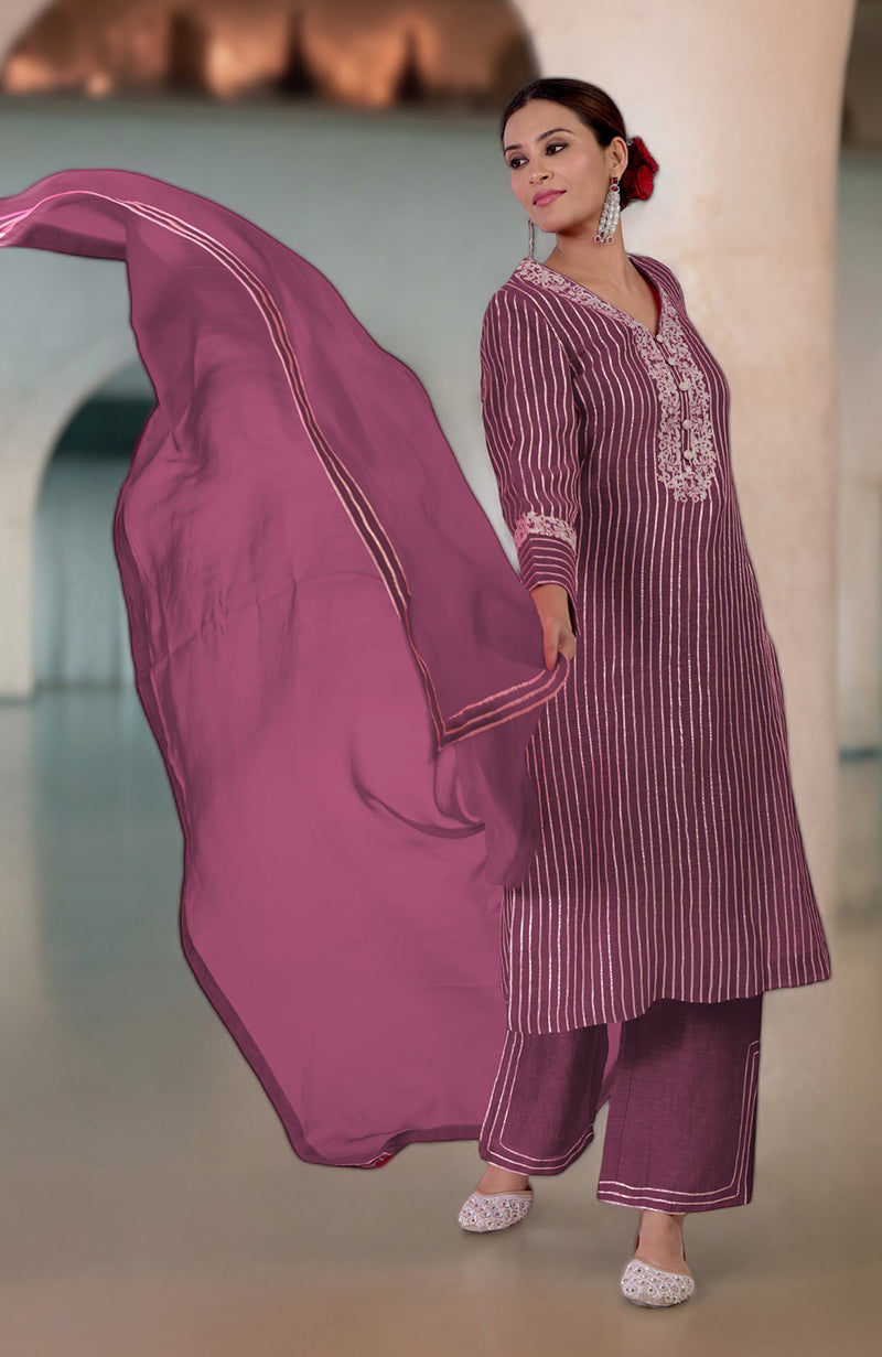 A woman models a burgundy purple silk linen suit with gota and tilla embroidery.