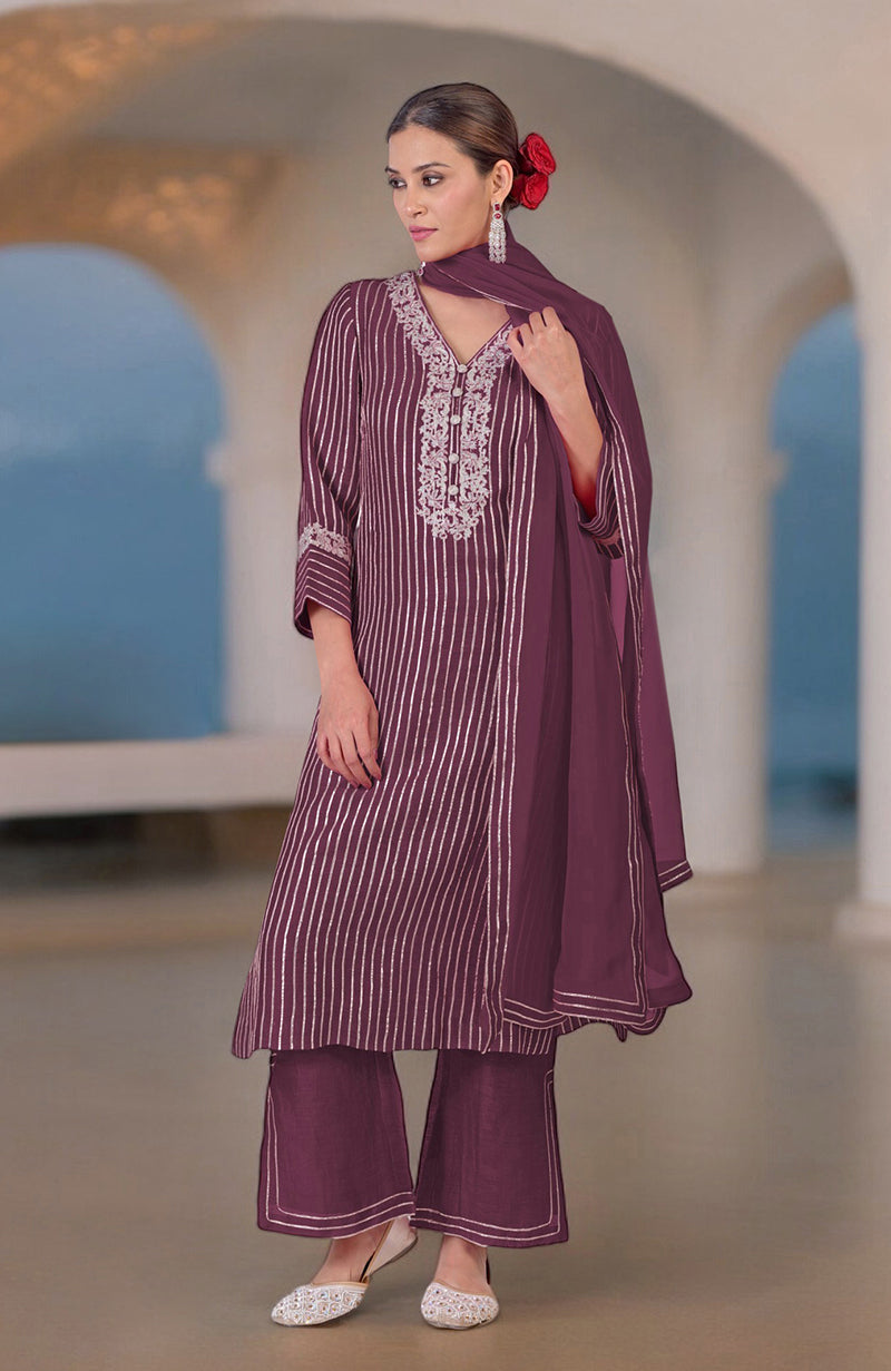 A woman models a burgundy purple silk linen suit with silver embroidery and stripes.