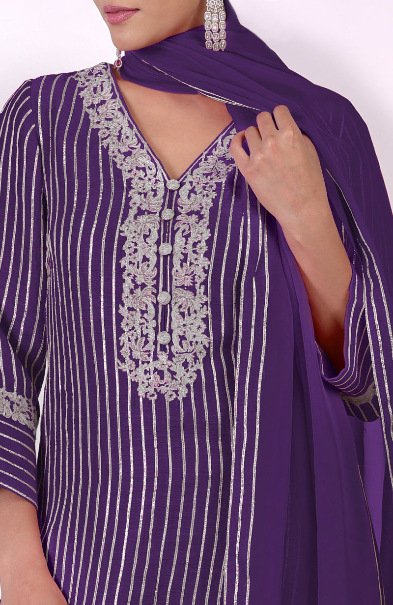 A woman models a purple silk linen suit with silver embroidery and vertical stripes.