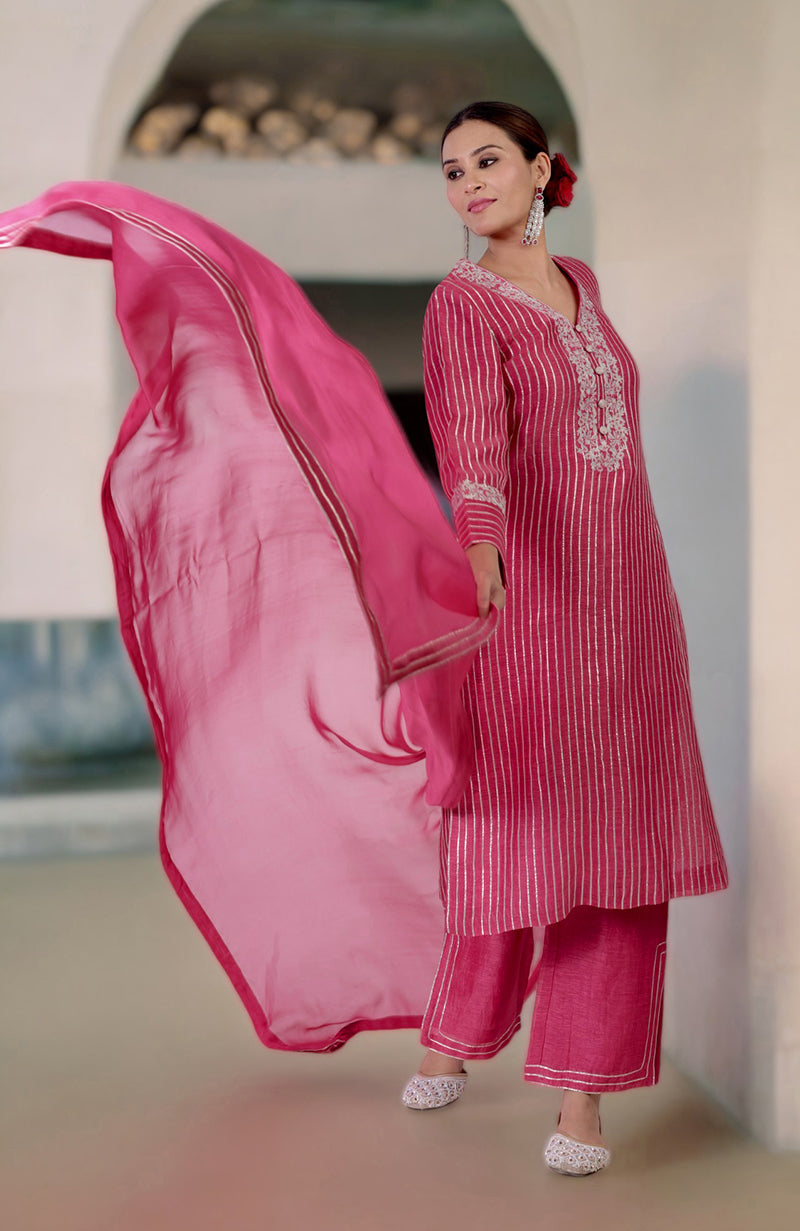 A woman models a pink linen silk suit with silver stripes and embroidery, holding a matching dupatta.