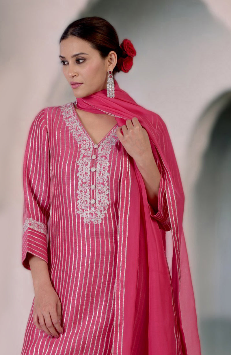A woman models a pink silk linen suit with silver embroidery and vertical stripes.