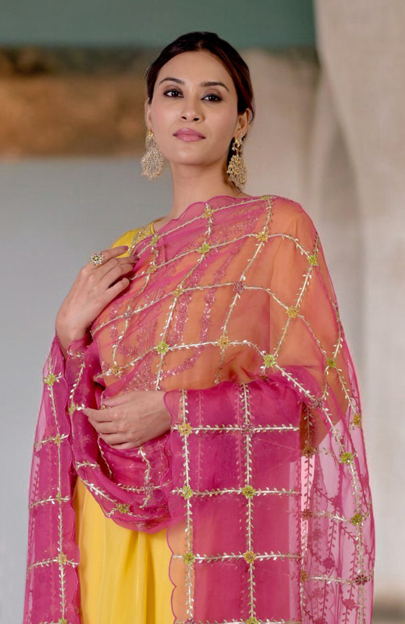 A woman in a buttercup yellow suit with a fuchsia dupatta featuring gota and zardozi work.