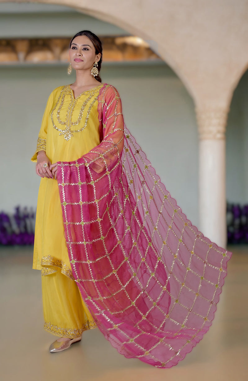 A woman models a buttercup yellow suit with gold embroidery and a fuchsia dupatta.