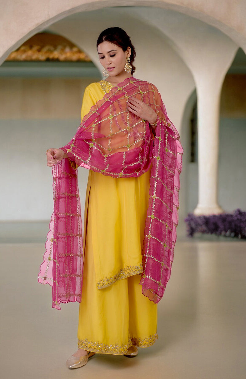 A woman models a buttercup yellow suit with a fuchsia dupatta.