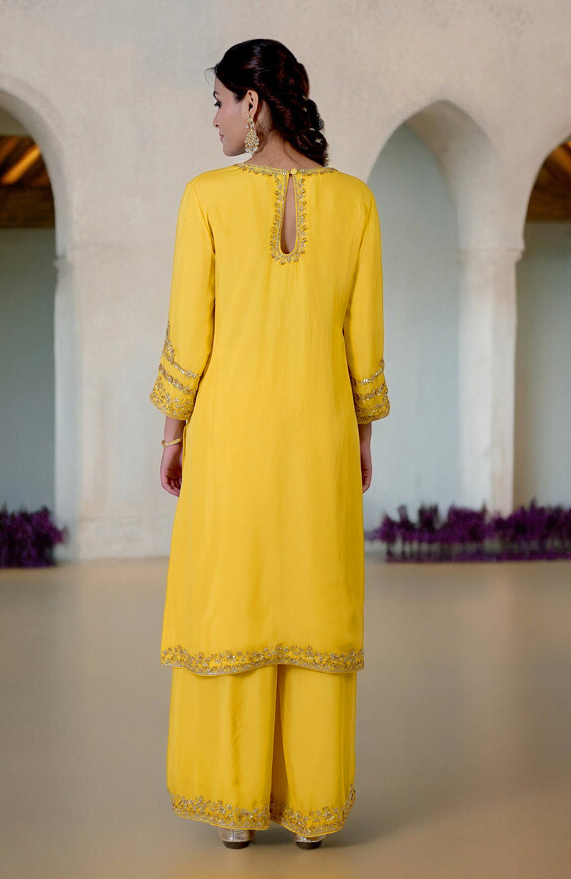 A woman models a buttercup yellow zardozi hand-embroidered suit set from the back.