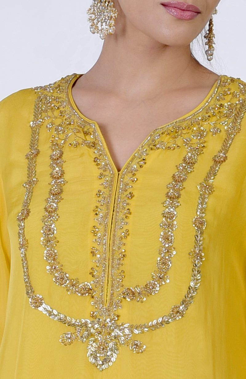 A woman wears a buttercup yellow suit with intricate gold zardozi embroidery.