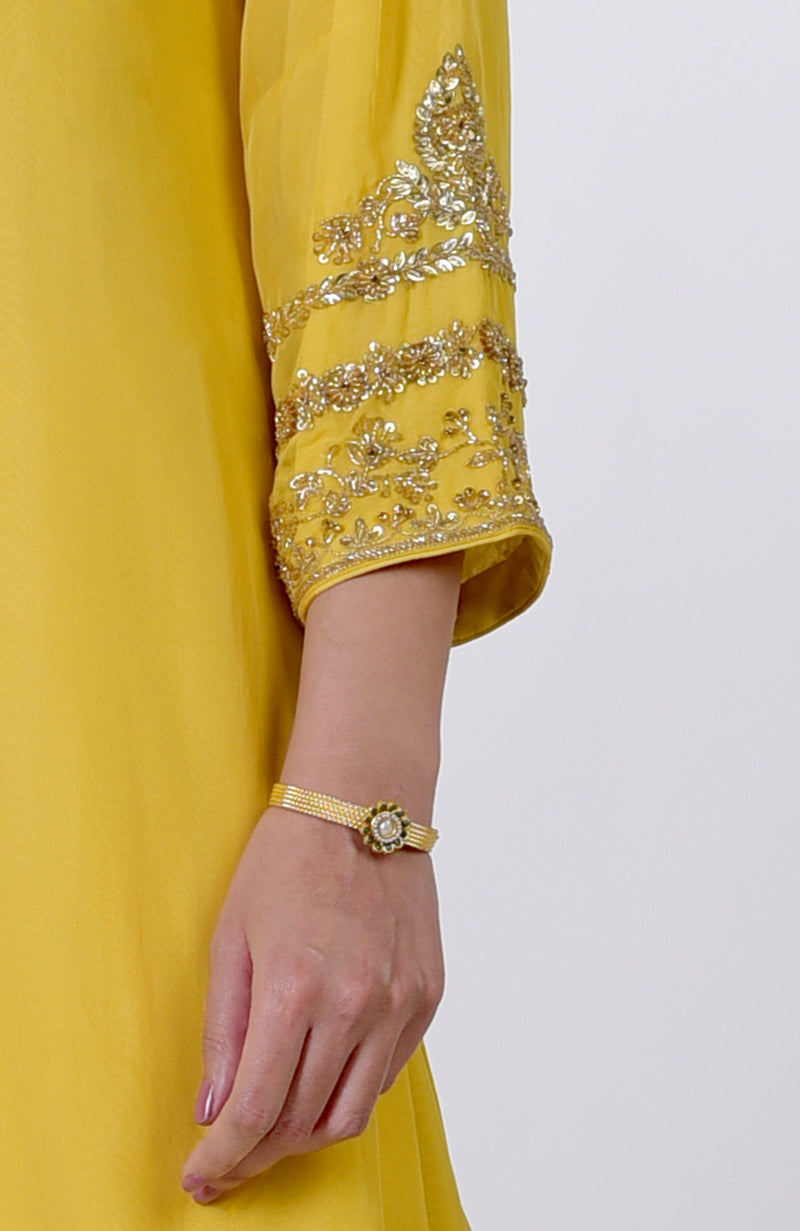 A woman's arm in a yellow embroidered suit with a gold bracelet.
