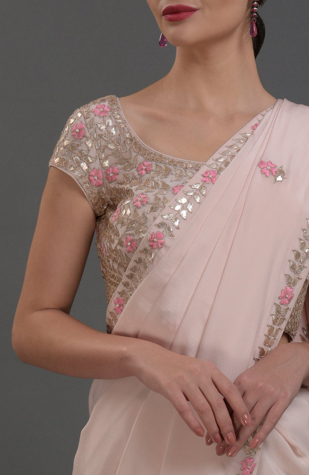 A woman models a nude pink saree with intricate gold and pink floral embroidery.