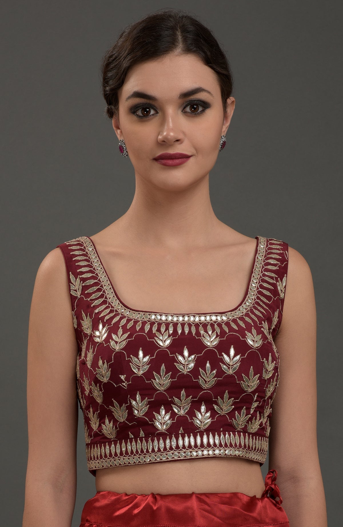 A woman models a burgundy embroidered gota patti blouse with a square neckline.