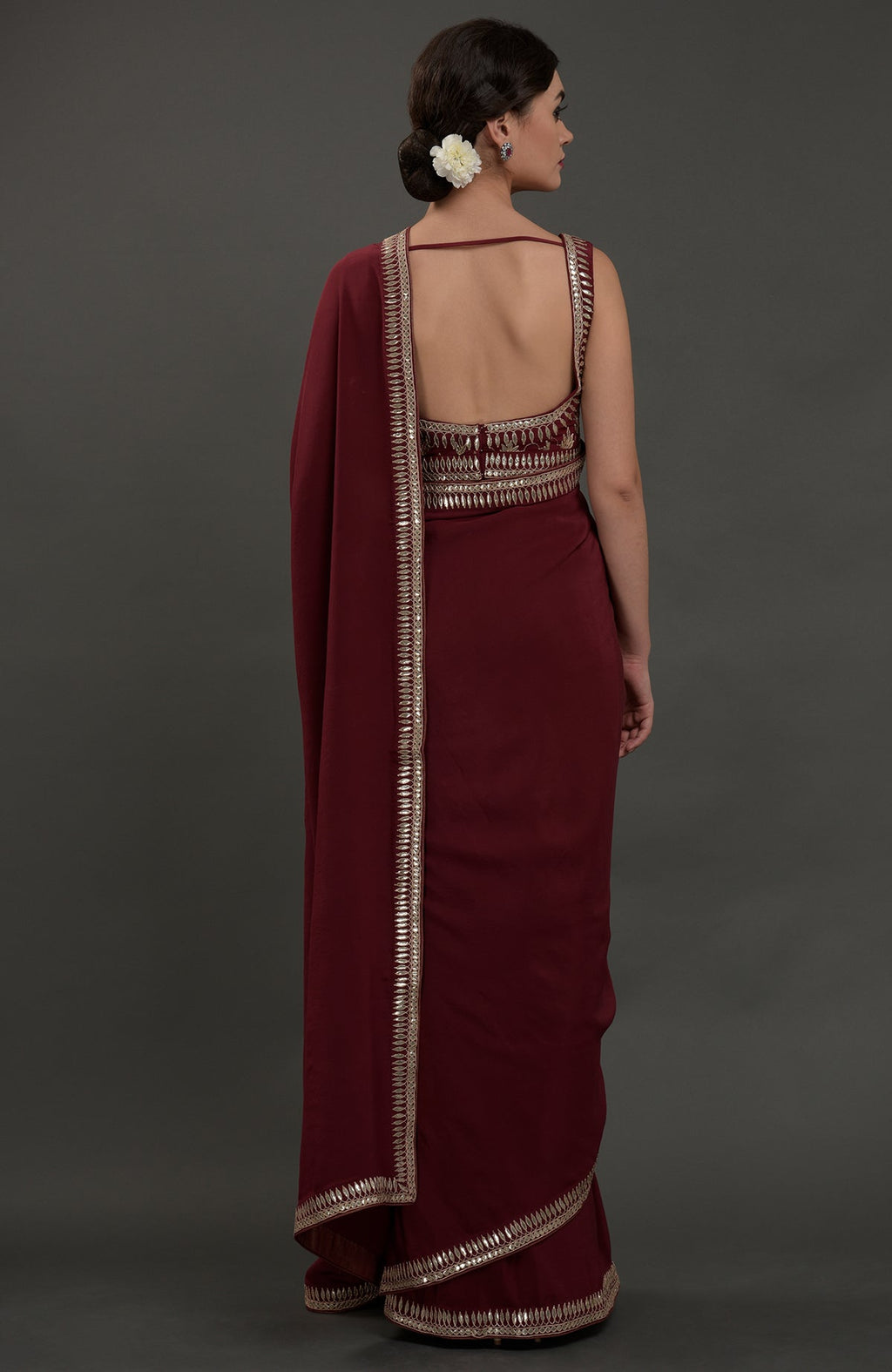 A woman from behind models a burgundy saree with intricate silvery gold gota patti embroidery.