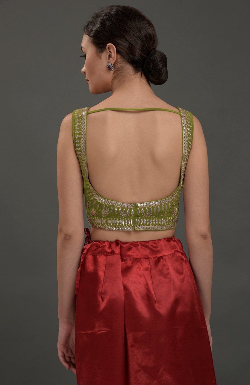 A woman from behind wears an avocado green embroidered blouse with a deep back and red skirt.
