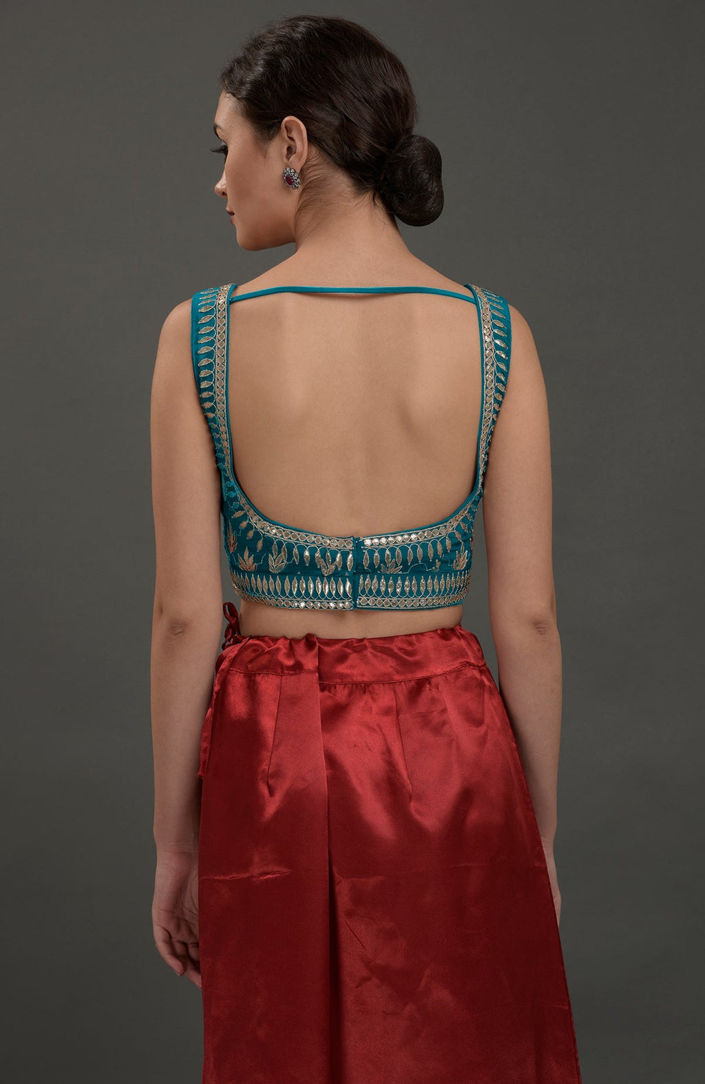 Woman in an oceanside blue embroidered blouse and a red skirt, viewed from the back.