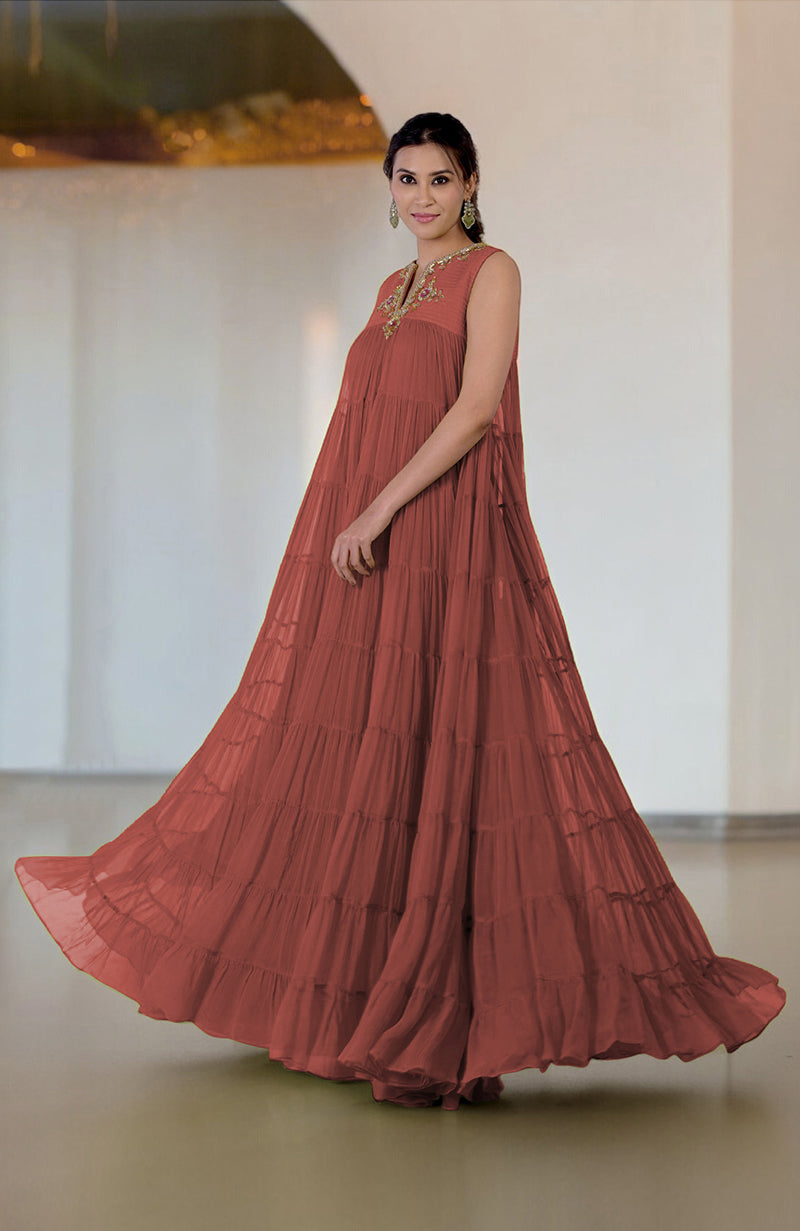 A woman models a rust-colored tiered dress with zardozi hand embroidery.