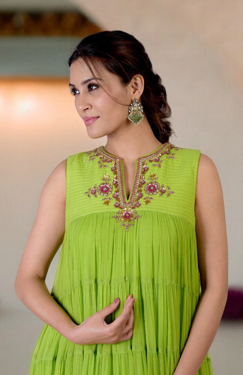 A woman models a green tiered dress with zardozi hand embroidery on the neckline.